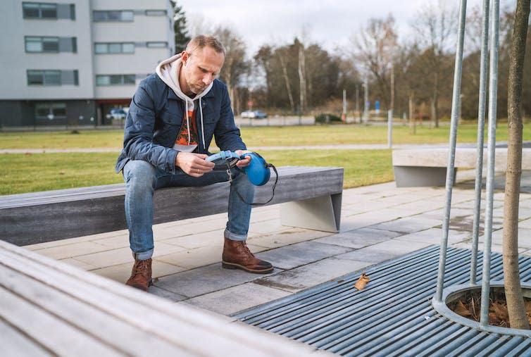 Man on bench looking at the ground holding a dog leash