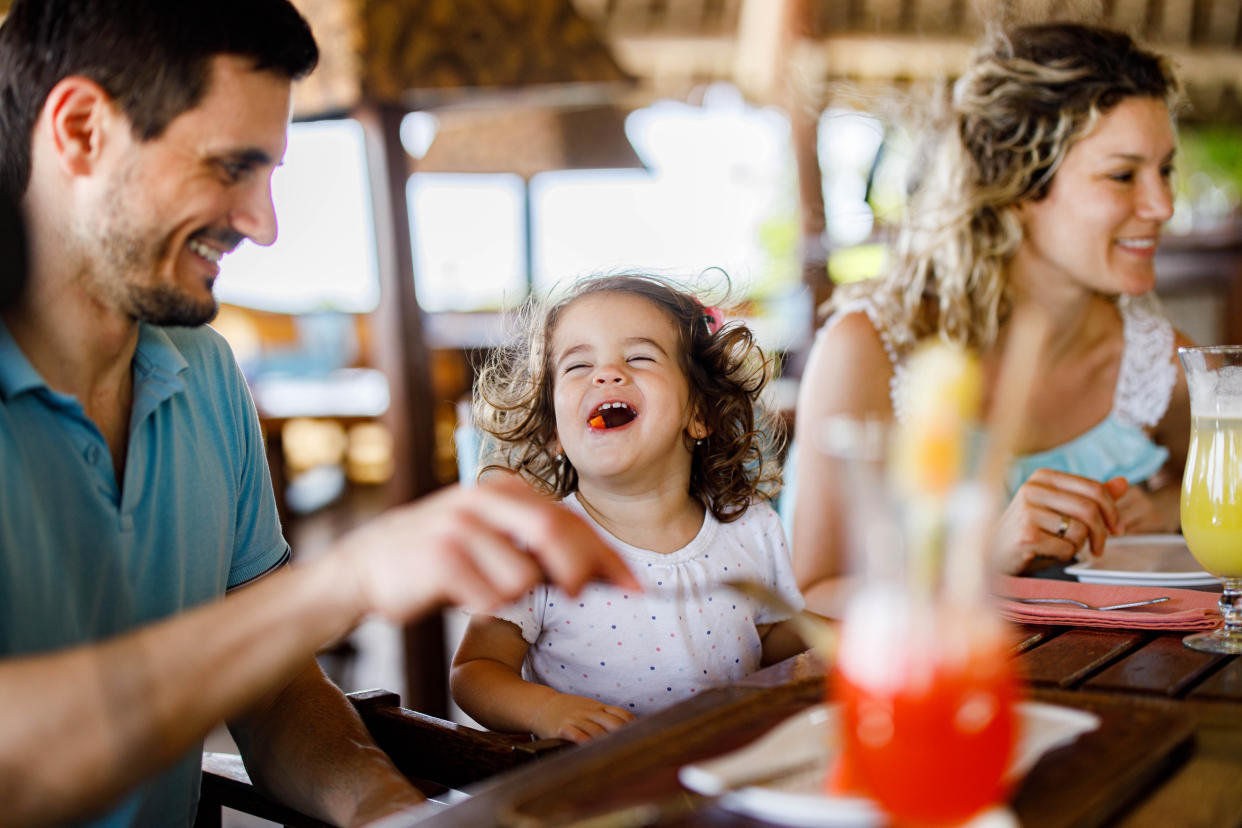 Happy girl having fun while eating lunch with her parents in a restaurant.