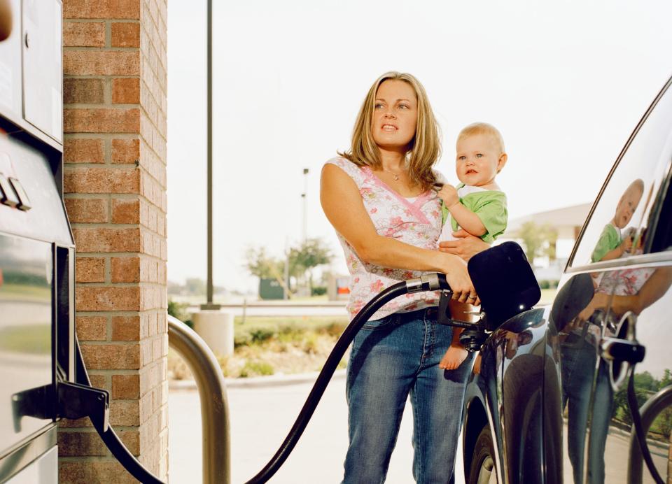 Woman pumps gas while holding a baby.