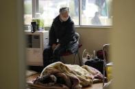 A woman sits next to another lying on a futon bed at a temporary evacuation center in Suzu in the Noto peninsula facing the Sea of Japan, northwest of Tokyo, Wednesday, Jan. 3, 2024, following Monday's deadly earthquake. (AP Photo/Hiro Komae)