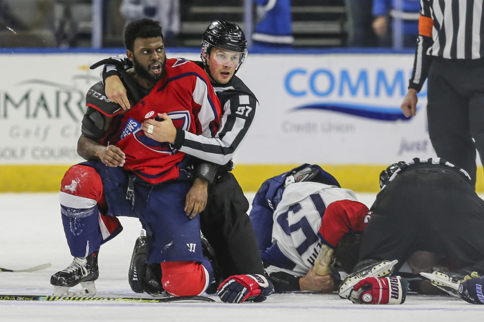 After an on-ice fight, South Carolina Stingrays defenseman Jordan Subban (5), left, is held by linesman Shane Gustafson while Jacksonville Icemen defenseman Jacob Panetta (15) is face-down on the ice engaged with another player during overtime of an ECHL hockey game in Jacksonville, Fla., Saturday, Jan. 22, 2022. The ECHL has suspended Panetta after the brother of longtime NHL defenseman P.K. Subban accused the Jacksonville defenseman of making “monkey gestures” in his direction. (AP Photo/Gary McCullough)