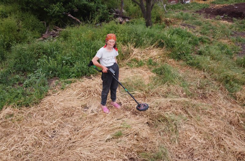 Local resident Hanna Plishchynska uses metal detector to find mines at a field near her house in the village of Stepova Dolyna