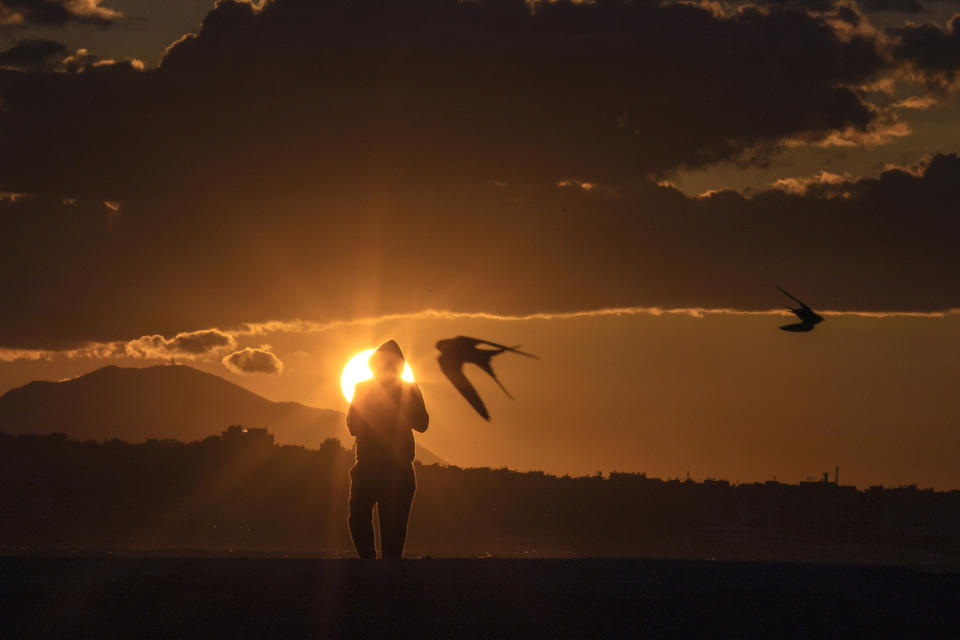 Birds fly as a man walks during a sunset in Alimos, a seaside suburb of Athens, on Tuesday, April 20, 2021. (AP Photo/Petros Giannakouris)