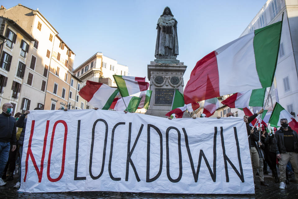 Demonstrators wearing masks with the colors of the Italian flag wave flags and hold a banner with writing reading "No Lockdown" during a protest against the government's restriction measures to curb the spread of COVID-19, in Rome's Campo dei Fiori Square, Saturday, Oct. 31, 2020. (Roberto Monaldo/LaPresse via AP)