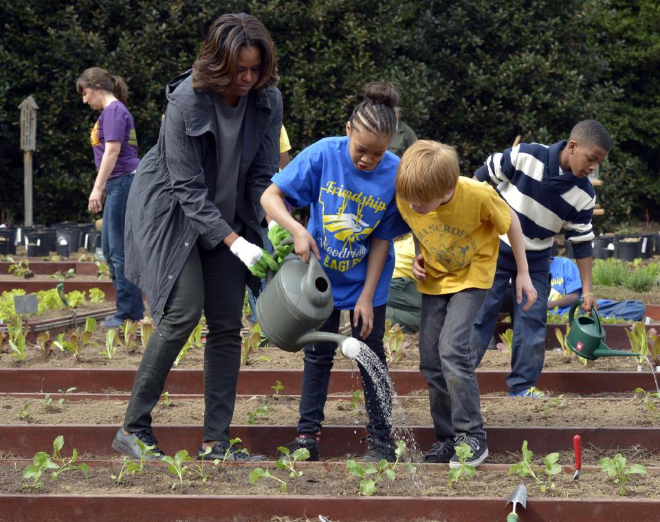 First lady Michelle Obama helps to hold a watering can after she and Friendship Public Charter Elementary School student Dynasty Meade, center, and Bancroft Elementary School student Silas Stutz, right, planted broccoli in the White House Kitchen Garden at the White House in Washington, Wednesday, April 2, 2014. (AP Photo/Susan Walsh)