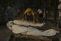 FILE - In this May 10, 2021, file photo, a man places wooden logs on the pyre during the cremation of people who died of COVID-19 at the Seemapuri crematorium in New Delhi, India. The World Health Organization said Monday, May 10, that a worrisome variant was first detected in India may spread more easily. Scientists are still trying to figure out if it resulted in the terrifying surge of infections in the nation, and looking to see if this could this happen elsewhere. (AP Photo/Ishant Chauhan, File)