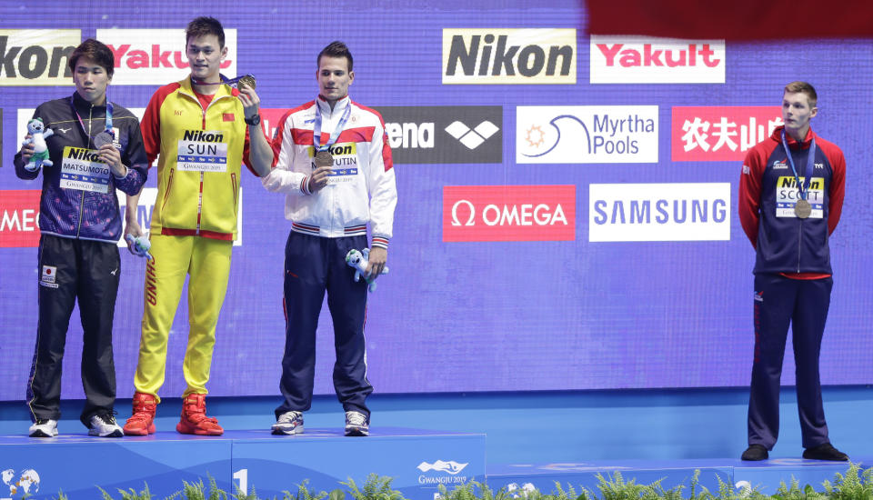 FILE - In this Tuesday, July 23, 2019 file photo, Britain's bronze medalist Duncan Scott, right, refuses to stand with gold medalist China's Sun Yang, second left, as silver winner Japan's Katsuhiro Matsumoto, left, and joint bronze medal winner Russia's Martin Malyutin pose on the podium following the men's 200m freestyle final at the World Swimming Championships in Gwangju, South Korea. One of China’s biggest Olympic stars will undergo a rare public trial of a doping case on Friday, Nov. 15, 2019 with his 2020 Tokyo Games place at stake. Three-time gold medalist swimmer Sun Yang is facing a World Anti-Doping Agency appeal in Switzerland that seeks to ban him for up eight years. (AP Photo/Mark Schiefelbein, File)