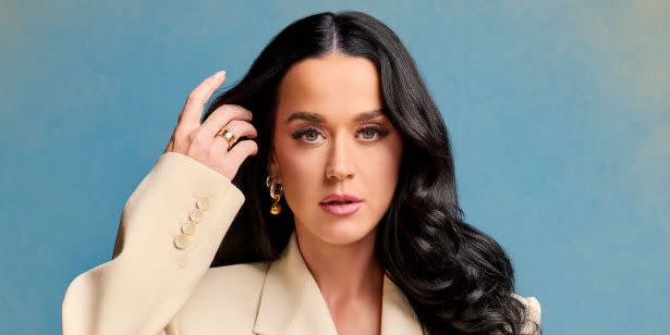 katy perry poses in a cream suit with her long hair down against a blue and yellow fade background