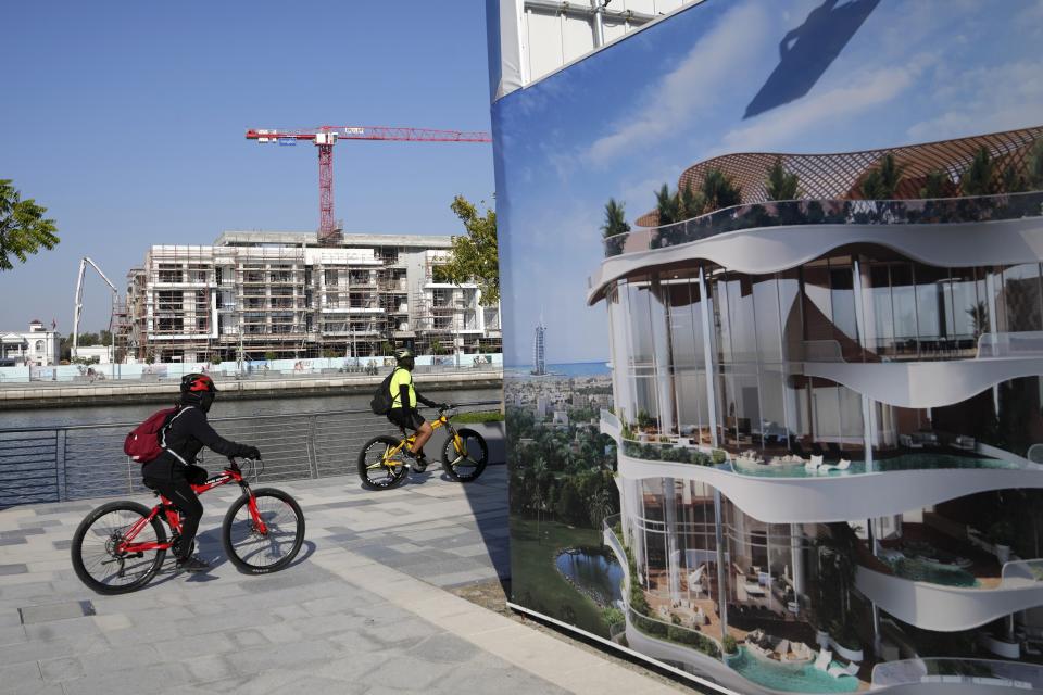 Bikers ride along the Dubai Water Canal while passing by an advertising billboard and a residential project in Dubai, United Arab Emirates, Tuesday, Jan. 31, 2023. For the first time since a 2009 financial crisis nearly brought Dubai to its knees, several major abandoned real estate projects now show signs of life. As with its other booms, war again is driving money into Dubai and buoying its economy. This time it's Russian investors fleeing Moscow’s war on Ukraine, rather than people escaping Mideast battlefields. (AP Photo/Kamran Jebreili)