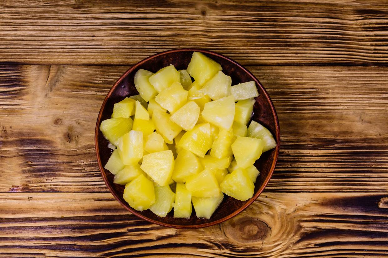 Ceramic plate with chopped canned pineapple on rustic wooden table. Top view