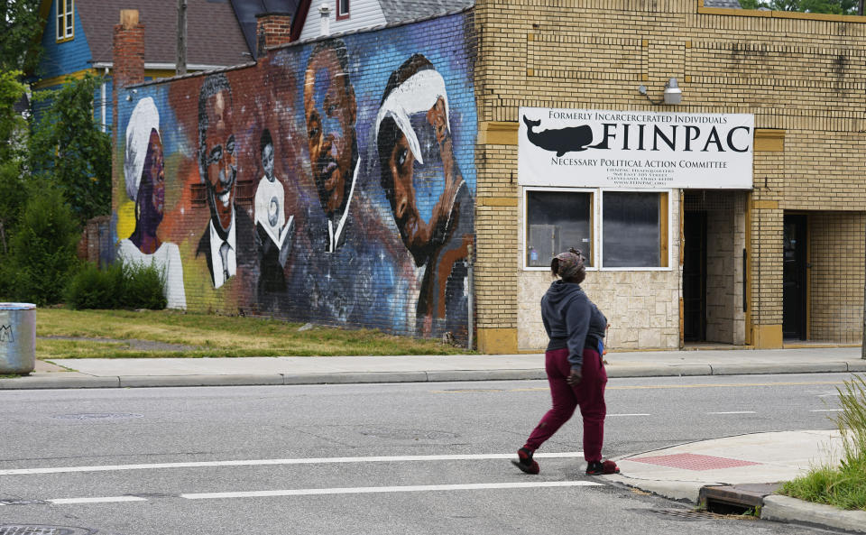 A woman walks past a mural painted on a near-empty street near MAC Pharmacy, Wednesday, May 29, 2024, in Cleveland. (AP Photo/Sue Ogrocki)