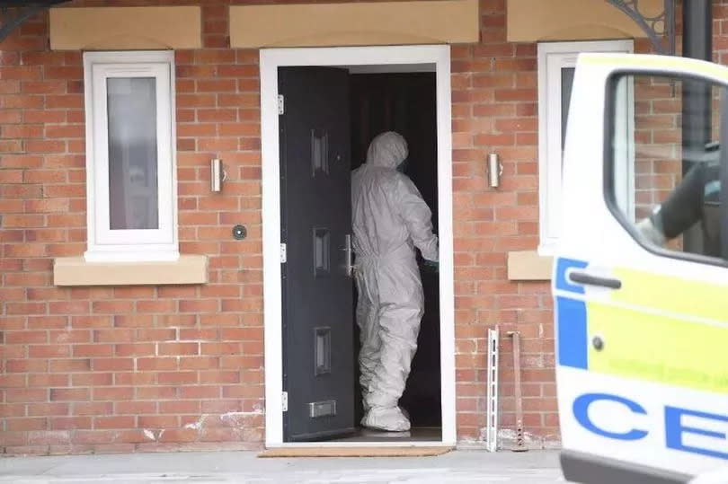 A forensic officer enters the house as police stand guard