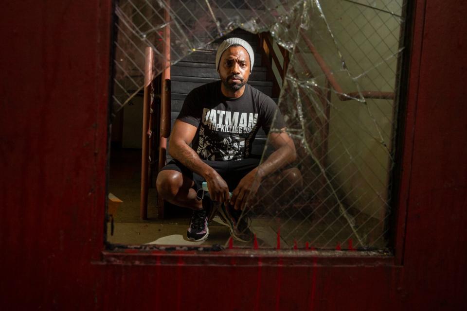 Jarian Jovan Banks, kneeling, is seen through a broken glass panel of an exit door at Sanborn Hotel Apartments.