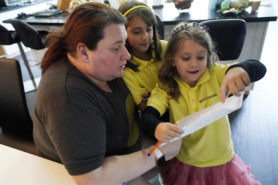 Anabelle Chao, right, shows her mother Erica, left, and her sister Emily, center, how she did on a writing exercise after finishing remote learning for the day, Thursday, Oct. 1, 2020, at their home in North Miami Beach, Fla. Rather than wait to see how the Miami-Dade school system would handle instruction this fall, Erica Chao enrolled her two daughters in a private school that seemed better positioned to provide remote learning than their public elementary school was when the coronavirus first reached Florida. (AP Photo/Wilfredo Lee)