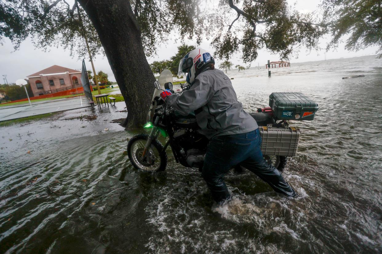 A man walks his motorcycle to Desoto Park after attempting to ride through an impassable South Bermuda Boulevard at Palmetto Beach (AP)