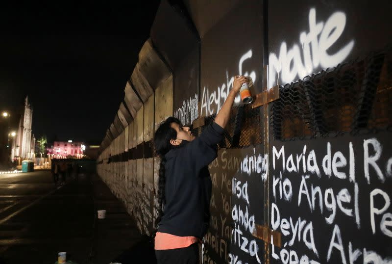 A woman paints the names of victims of femicide in Mexico on fences placed outside the National Palace ahead of a Women's Day protest, in Mexico City