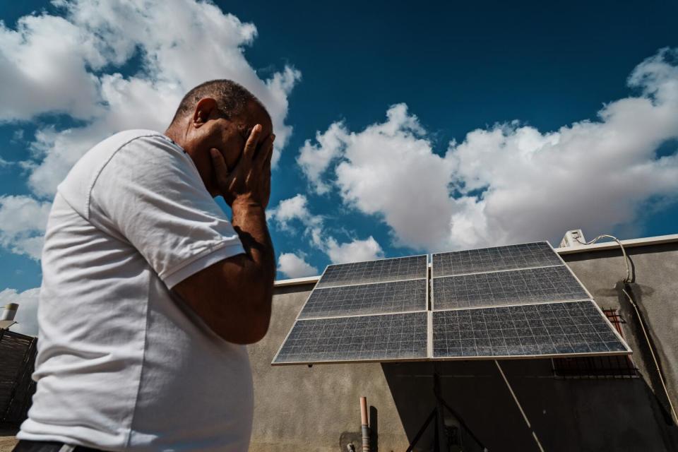 A man in a white shirt covers his face with his hand as he walks by a solar panel