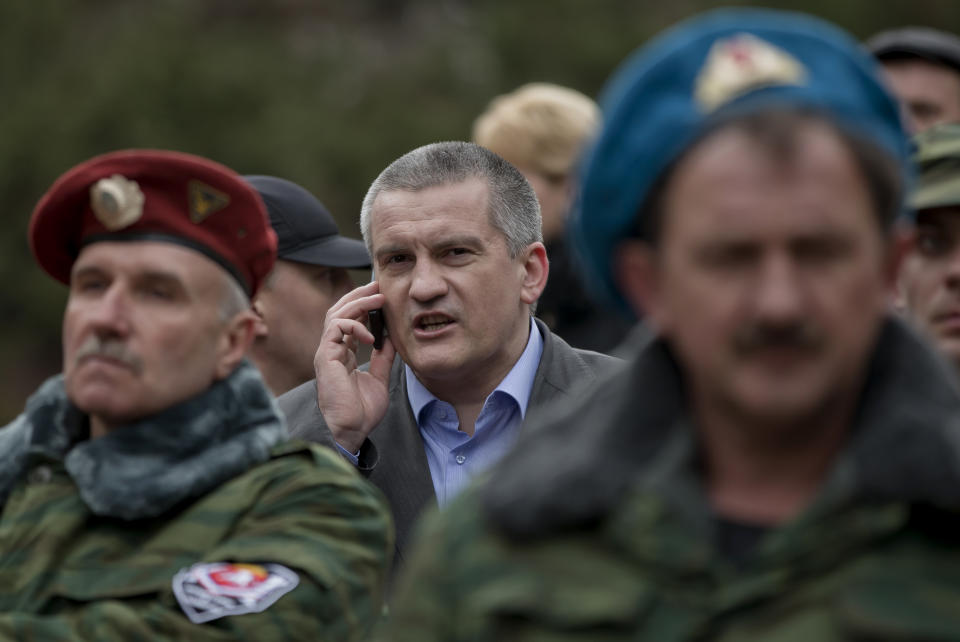 FILE - In this Saturday, March 8, 2014 file photo, Crimean Premier Sergei Aksyonov, center, speaks on a mobile phone as he attends the swearing in ceremony for the first unit of a pro-Russian armed force, dubbed the "military forces of the autonomous republic of Crimea" in Simferopol, Ukraine. Aksyonov, the head of Crimea's unrecognized Russian-backed government, has said Ukrainian solders will be allowed to surrender peacefully, leave the Crimea altogether or resign from the armed forces. (AP Photo/Vadim Ghirda, file)