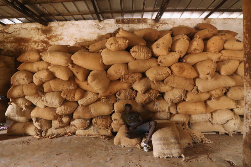 A worker sits near a pile of sacks of cocoa at a warehouse in Soubre,