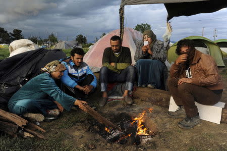 Migrants and refugees gather by a fire at a makeshift camp at the Greek-Macedonian border near the village of Idomeni, Greece, April 25, 2016. REUTERS/Alexandros Avramidis