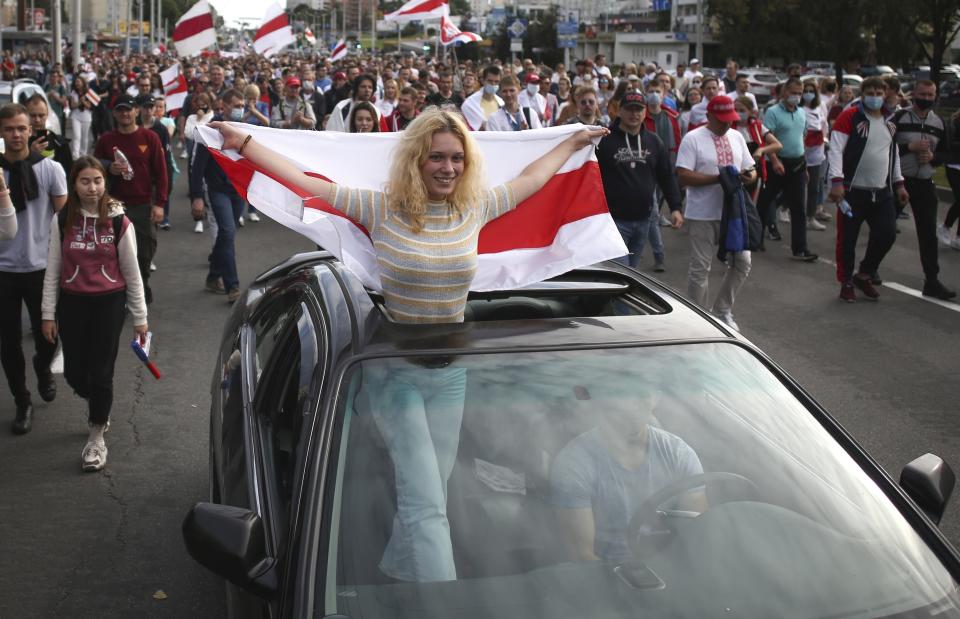 A woman standing in a car, waves an old Belarusian national flag, during a Belarusian opposition supporters' rally protesting the official presidential election results in Minsk, Belarus, Sunday, Sept. 13, 2020. Protests calling for the Belarusian president's resignation have broken out daily since the Aug. 9 presidential election that officials say handed him a sixth term in office. (Tut.by via AP)