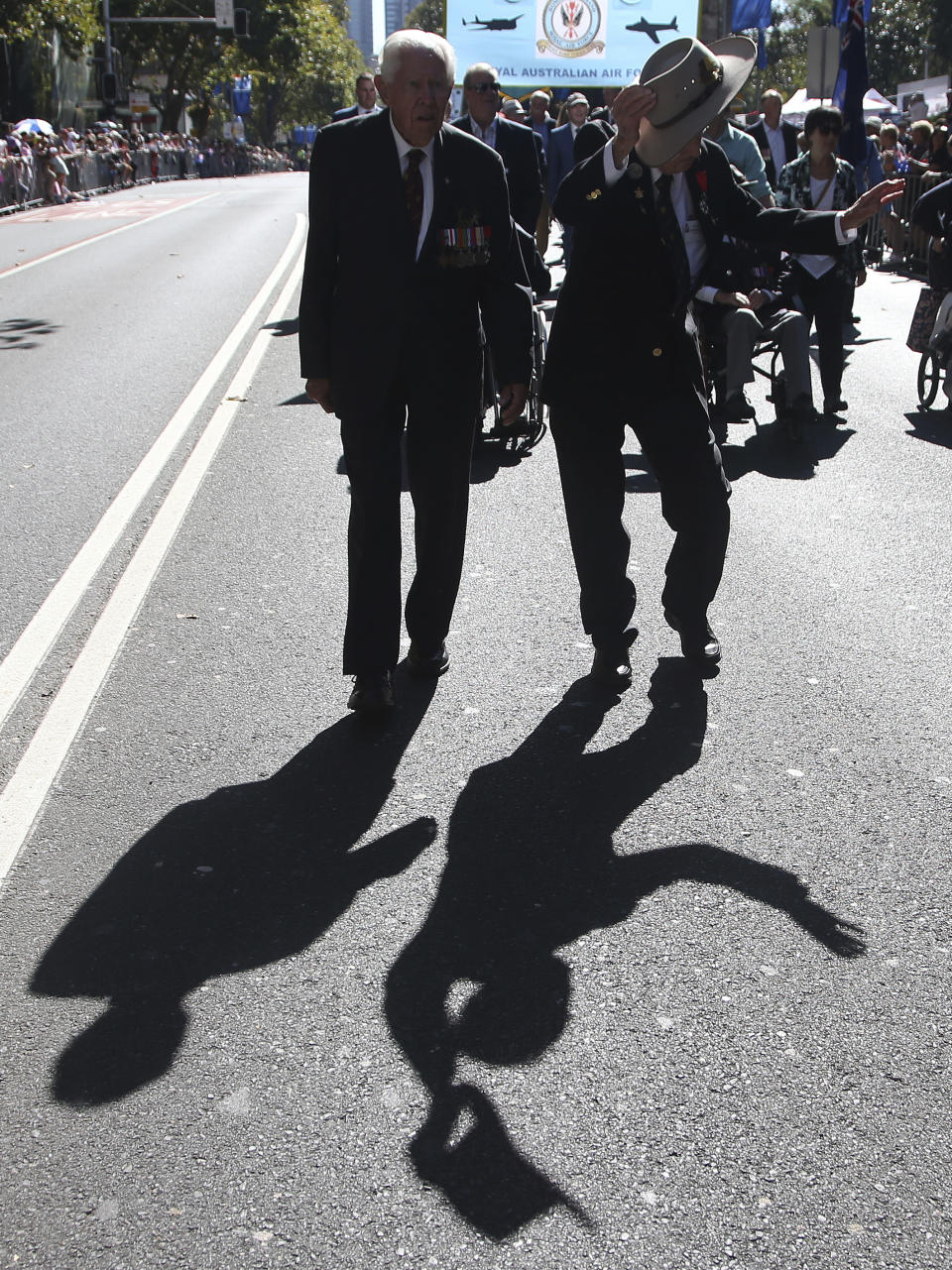 The shadow of an Australian veteran, right, is cast on the ground as he waves his hat during a march celebrating ANZAC Day, a national day of remembrance in Australia and New Zealand that commemorates those that served and died in all wars, conflicts, and while peacekeeping, in Sydney, Australia, Thursday, April 25, 2019. (AP Photo/Rick Rycroft)