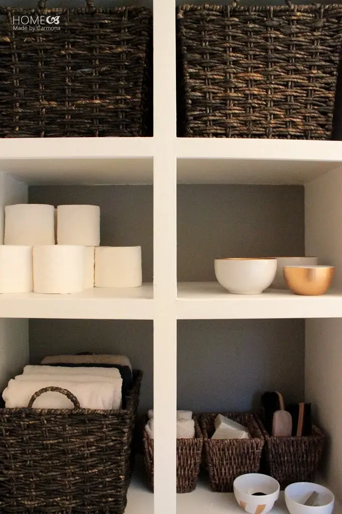 six open cubby hole cabinets with baskets fill with towels and other items bowls and toilets paper on the various shelves