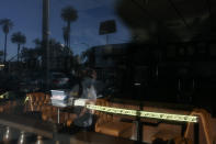 A man wearing a mask is reflected in the window of a restaurant with caution tape around its booths amid the coronavirus pandemic in the Westlake neighborhood of Los Angeles, Thursday, May 21, 2020. While most of California took another step forward to partly reopen in time for Memorial Day weekend, Los Angeles County didn't join the party because the number of coronavirus cases has grown at a pace that leaves it unable to meet even the new, relaxed state standards for allowing additional businesses and recreational activities. (AP Photo/Jae C. Hong)