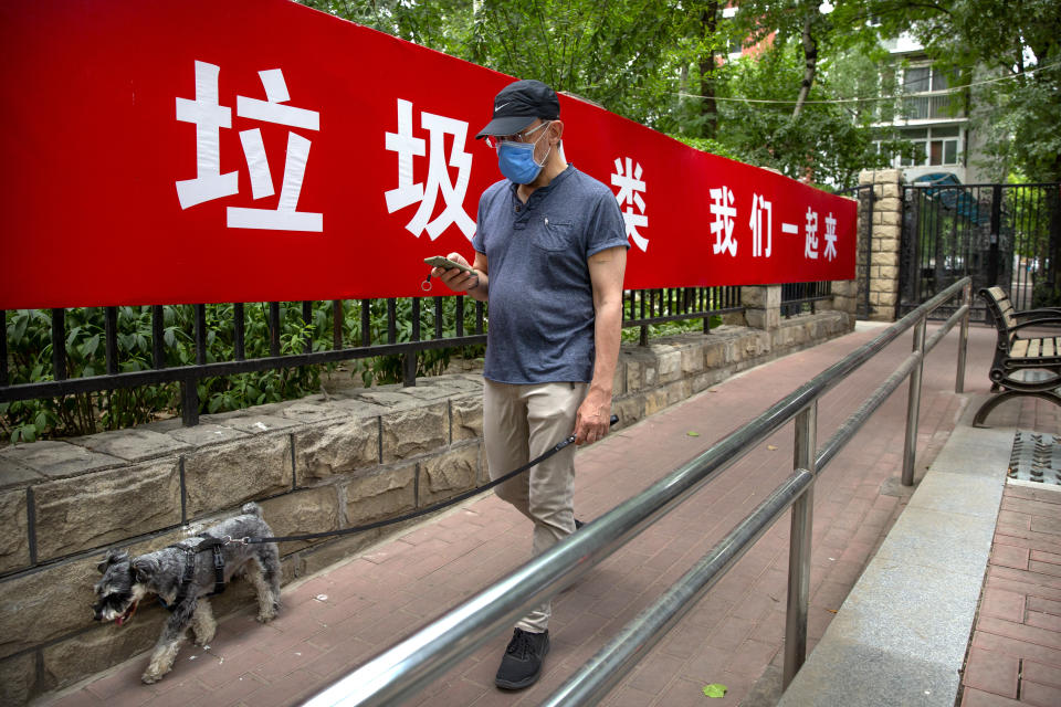 A man wearing a face mask to protect against the spread of the new coronavirus walks past a propaganda banner encouraging people to sort their garbage in Beijing, Wednesday, June 24, 2020. New virus cases have declined in China and in the capital Beijing, where a two-week spike appears to be firmly waning. (AP Photo/Mark Schiefelbein)