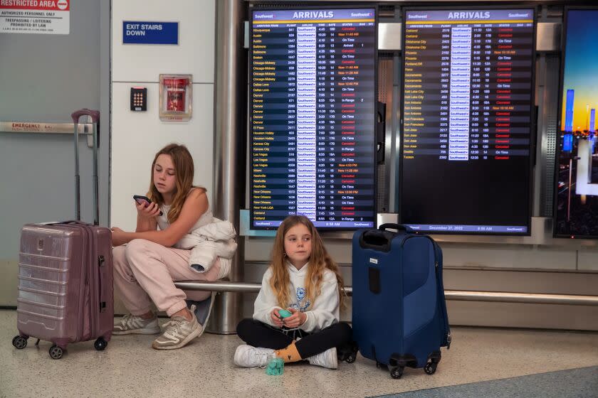 Los Angeles, CA - December 27: Zoe Schelter, 12, and 9-year-old Milo Schelter wait for their mother went to take care of ticket refunds after Southwest Airlines canceled their from Oakland to Los Angeles yesterday. Schelters drove from Oakland and came to LAX Southwest Terminal 1 to collect their luggage on Tuesday, Dec. 27, 2022 in Los Angeles, CA. (Irfan Khan / Los Angeles Times)