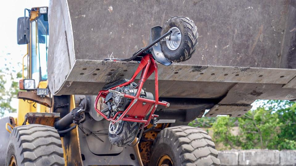 A front-loader holds a mini-bike by the handlebars at Thursday's news conference.