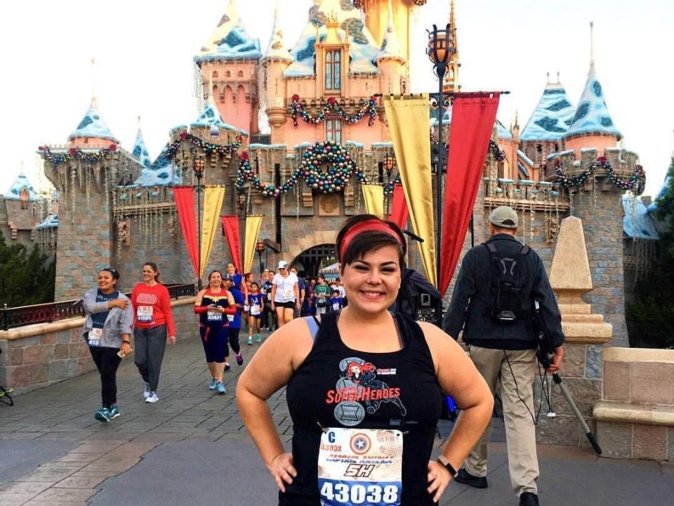 dana posing in a running bib in front of sleeping beauty castle at disneyland