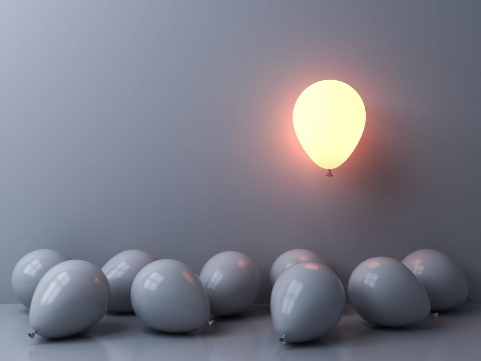 Gray balloons with one lit-up one rising above them