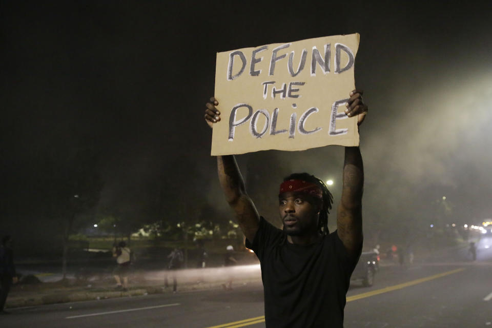 A man holds up a sign amid smoke of a fire during a protest Saturday, June 13, 2020, near the Atlanta Wendy's where Rayshard Brooks was shot and killed by police Friday evening following a struggle in the restaurant's drive-thru line in Atlanta. (AP Photo/Brynn Anderson)