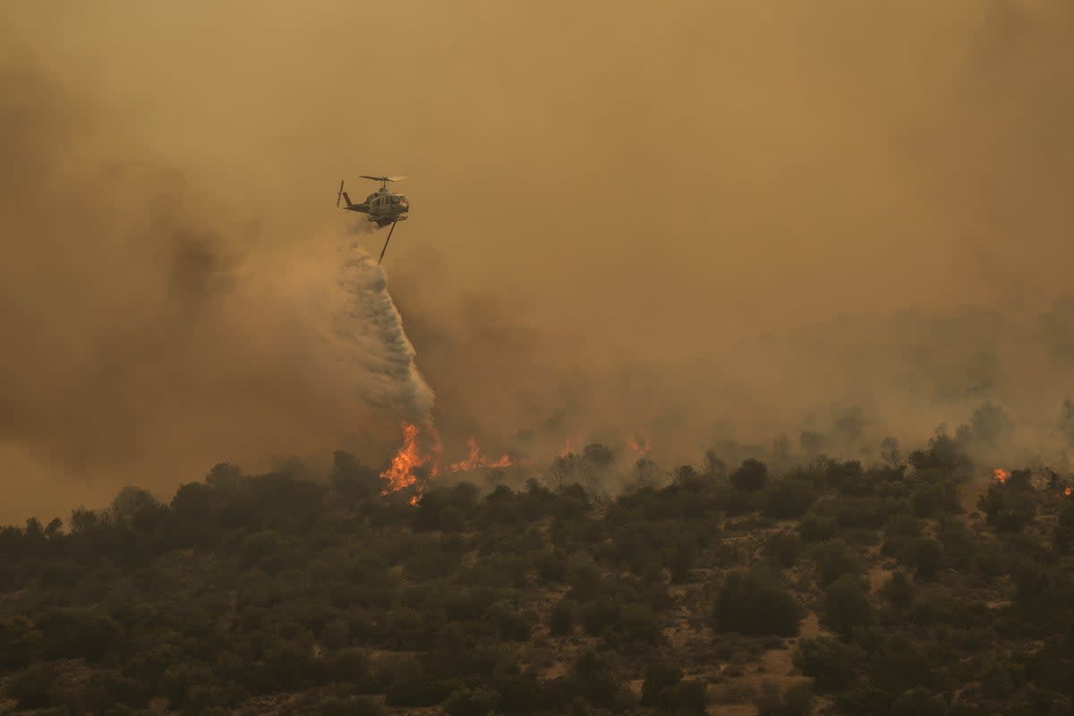 A firefighting helicopter dumps water in Mandra, west of Athens, on 18 July 2023. Another heatwave is expected to hit Greece today (AP)