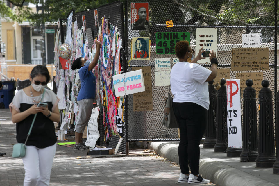 People look at protest posters that adorn the last remaining anti-scaling fencing surrounding a small building in Lafayette Park, Tuesday, June 16, 2020, near the White House in Washington, where protests have occurred over the death of George Floyd, a black man who was in police custody in Minneapolis. The rest of the park is open. (AP Photo/Jacquelyn Martin)