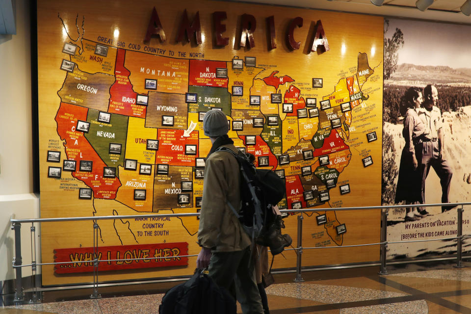 FILE - In this Nov. 21, 2018, file photo, travelers pass by a map of the United States on the way to a security checkpoint at Denver International Airport in Denver. Thanksgiving travel is an ordeal under the best of circumstances, and a one-two punch of bad weather threatens to make it even more exhausting. There's a forecast for heavy snow in Denver, and another storm will crash into the West Coast, possibly fouling flights and making driving treacherous. (AP Photo/David Zalubowski, File)