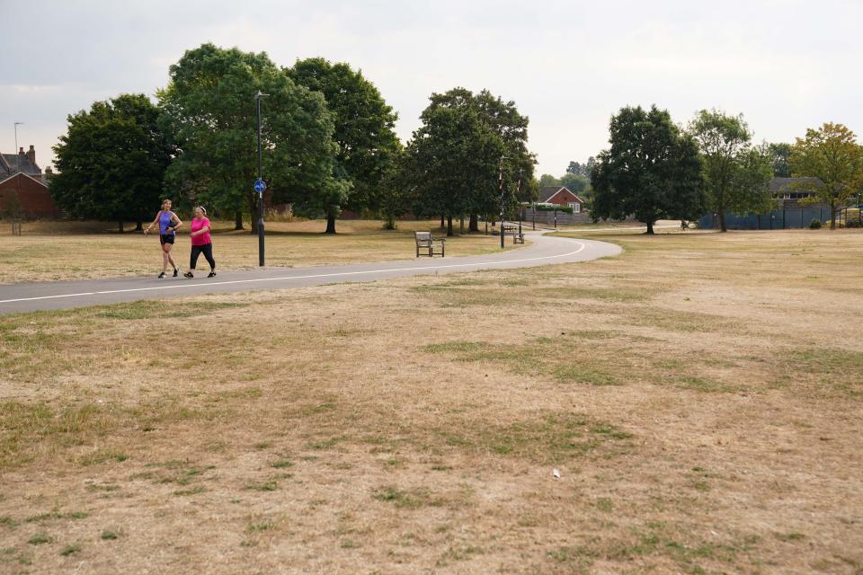 People walk by parched grass at St Nicholas' Park in Warwick, as the UK braces for three days of rain and yellow weather warnings. Picture date: Monday August 15, 2022.