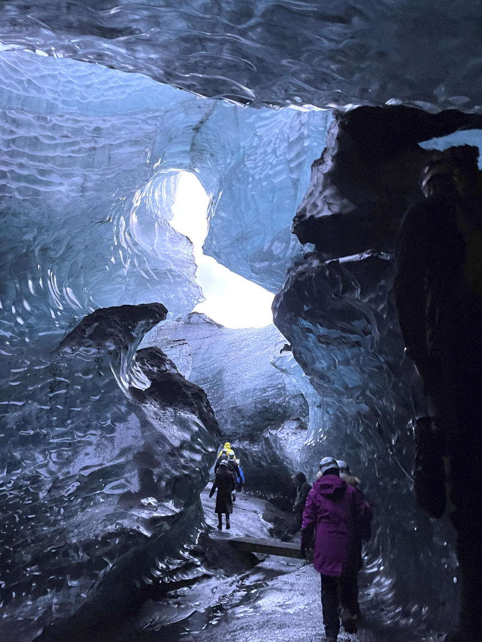 This Nov. 18, 2023 image provided by Beth Harpaz shows visitors walking through an ice cave at Vatnajokull National Park, located on an ice field in southeastern Iceland. The caves can only be explored on a tour with a registered guide. Winter crampons must be attached to shoes and boots for traction to avoid slipping. (Beth Harpaz via AP)