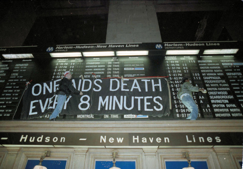 FILE - In this Tuesday, Jan. 24, 1991 file photo, members of the group Act-Up hang a banner across the train schedule board in New York's Grand Central Terminal. Hundreds of protesters marched through the station during rush hour to protest what they perceive as unfair spending for the war over AIDS treatment. (AP Photo/Ron Frehm, File)