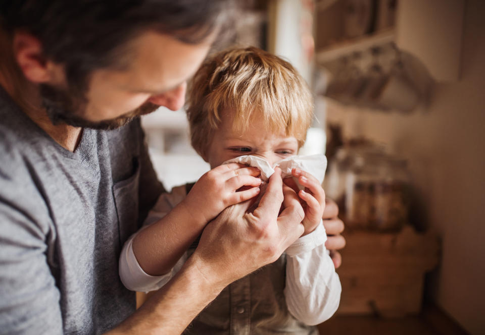 A father helps his toddler blow his nose.