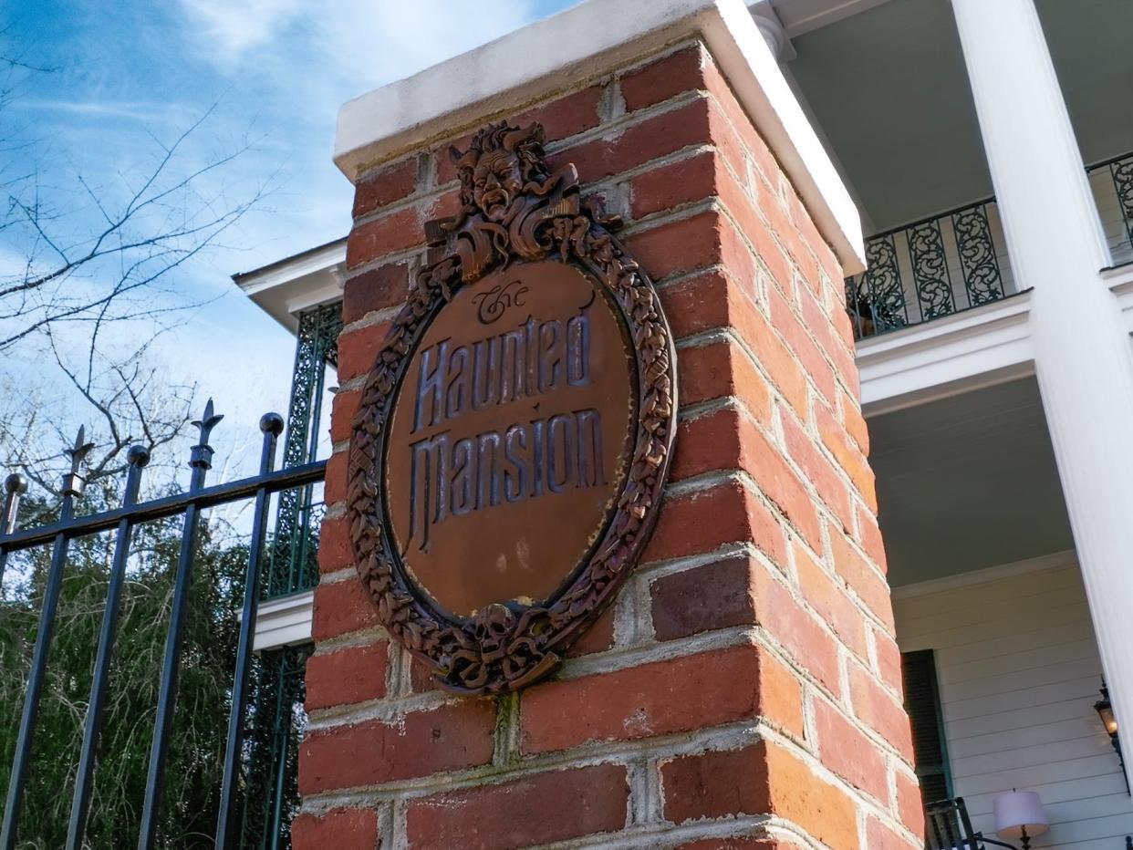 A sign that says "The Haunted Mansion" on a gate.