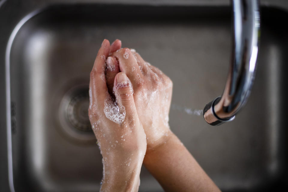 Close-up of hands being washed under running water in a sink, with soap bubbles visible