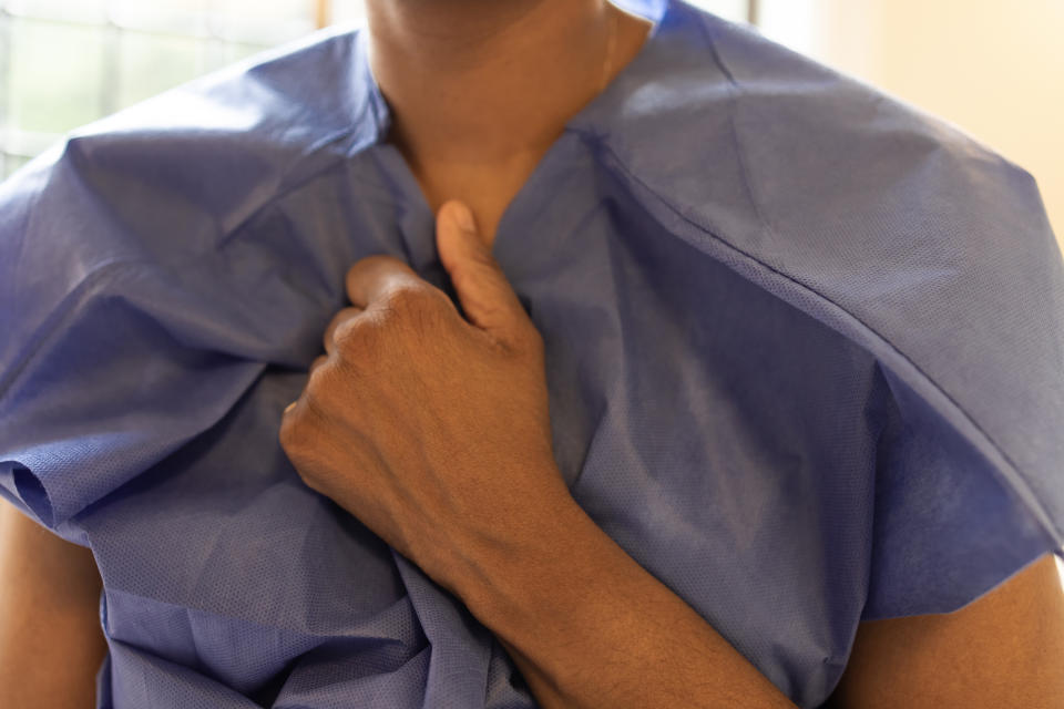 Person's hand gripping the front of a blue medical gown, upper body visible. No text or identifiable individuals present