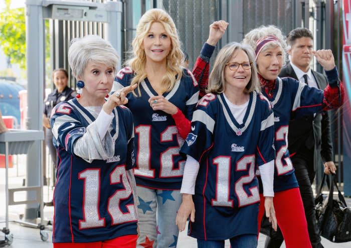 Rita, Jane, Sally, and Lily wearing patriots jerseys walking through security at a stadium