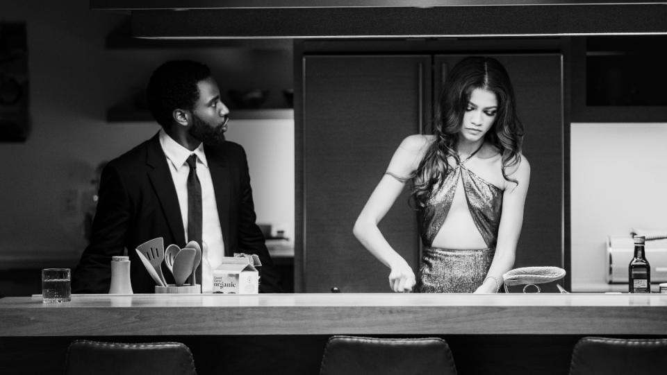 Malcolm and Marie film a woman in a dress stands at a counter cutting butter while a man in a suit looks on