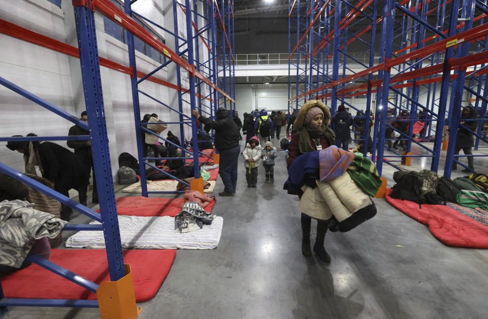 Migrants settle for the night in the logistics center in the checkpoint "Kuznitsa" at the Belarus-Poland border near Grodno, Belarus, on Tuesday, Nov. 16, 2021. Polish border forces say they were attacked with stones by migrants at the border with Belarus and responded with a water cannon. The Border Guard agency posted video on Twitter showing the water cannon being directed across the border at a group of migrants in a makeshift camp. (Maxim Guchek/BelTA via AP)