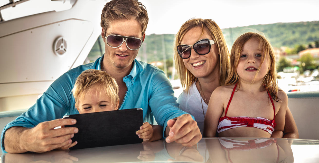 parents and two kids on boat look at tablet