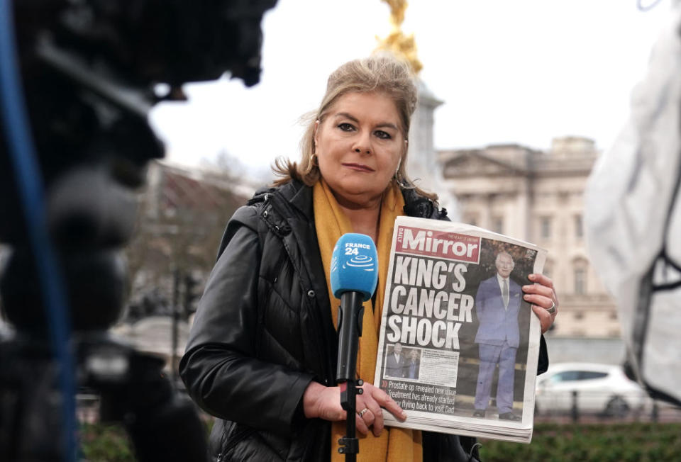 Reporter on location holding up a "Mirror" newspaper with a headline about a king's health