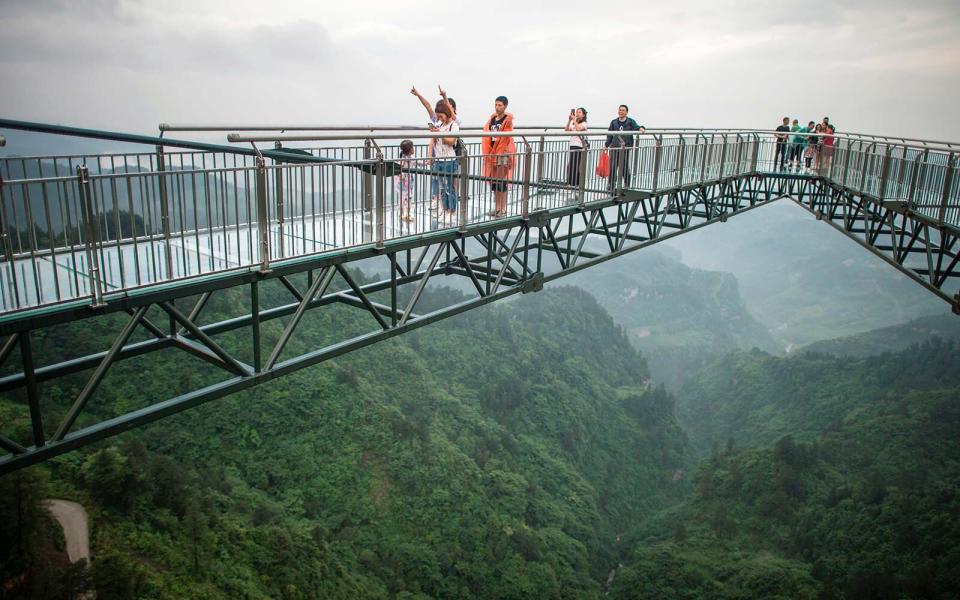 Tourists look on from a glass-bottomed skywalk.